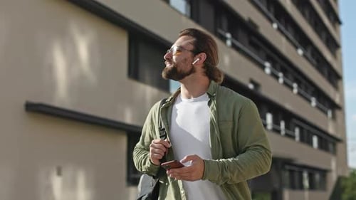Brunette Man with Earphones and Sunglasses Carrying Backpack Admiring Building