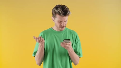 Frustrated Young Adult Using Smartphone on Yellow Background