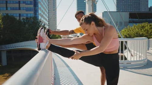 Smiling Woman Stretching Leg Aided by Man on Bridge