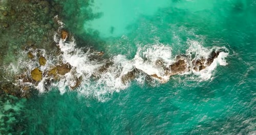 Turquoise ocean water crashing on surface rock and coral. Birdseye dolly