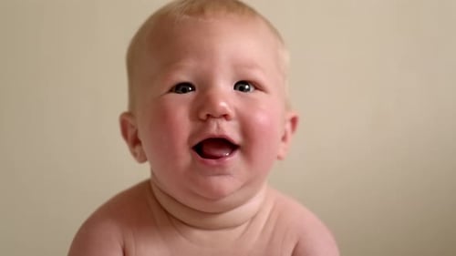 Lächelndes Säuglingsbaby liegt auf dem Bauch und schaut mit strahlenden Augen nach oben. Das Kindergesicht drückt pure Freude aus und
