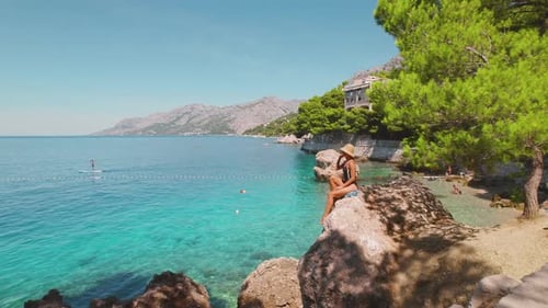 Woman sunbathing on stunning rocky coast of Brela in Croatia. Crystal clear sea waters and vibrant l