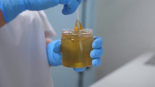 Technician Stirring Translucent Yellow Liquid in a Jar