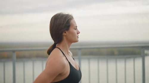 Woman Jogging in Black Neck Top Along Iron Fence By River for Fitness