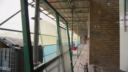 Chantier de construction avec échafaudage et panneaux de verre adossés à un mur de briques.