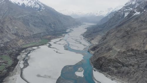 Aerial View of a Serene River Flowing Through a Snowy Mountain Valley in Pakistan Highlighting the