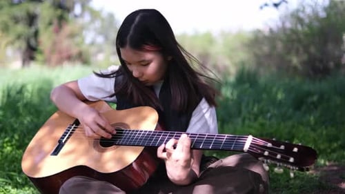 Girl Plays Guitar Outdoors in Grassy Field
