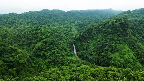A stunning waterfall cascading down the green mountains, surrounded by lush vegetation. The flowing