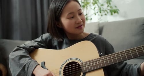 Asian Girl Playing Acoustic Guitar Music Instrument at Home Sitting on Floor Close Up