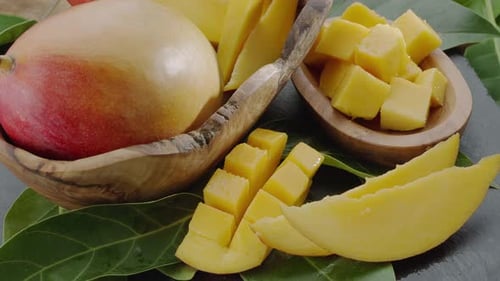 Ripe mango fruits with slices and mango leaves slowly move in the frame.