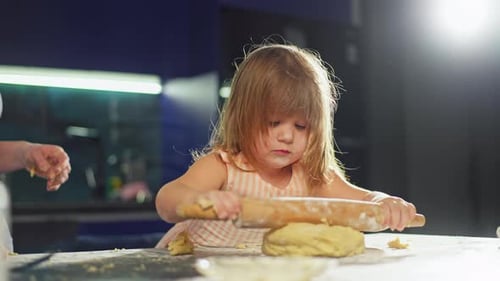 A Little Girl Rolls Out the Dough in the Kitchen