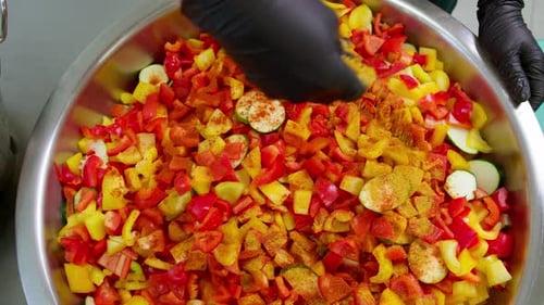 Close-up from above of a chef sprinkling curry spice over chopped vegetables in a large pot in slow