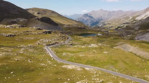 Un paysage montagneux à couper le souffle traversé par une route, le Drone descend lentement et démontre