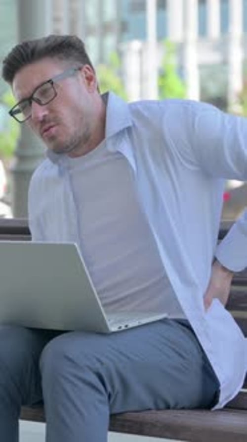 Man Working on Laptop Experiences Back Pain Outdoors