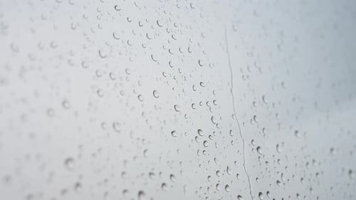 Une vue étroite de fortes gouttes de pluie est visible à travers une vitre.