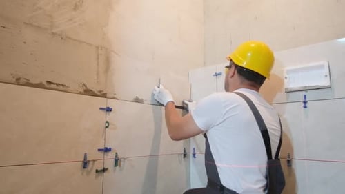 Man Installing Beige Tiles in Bright Bathroom