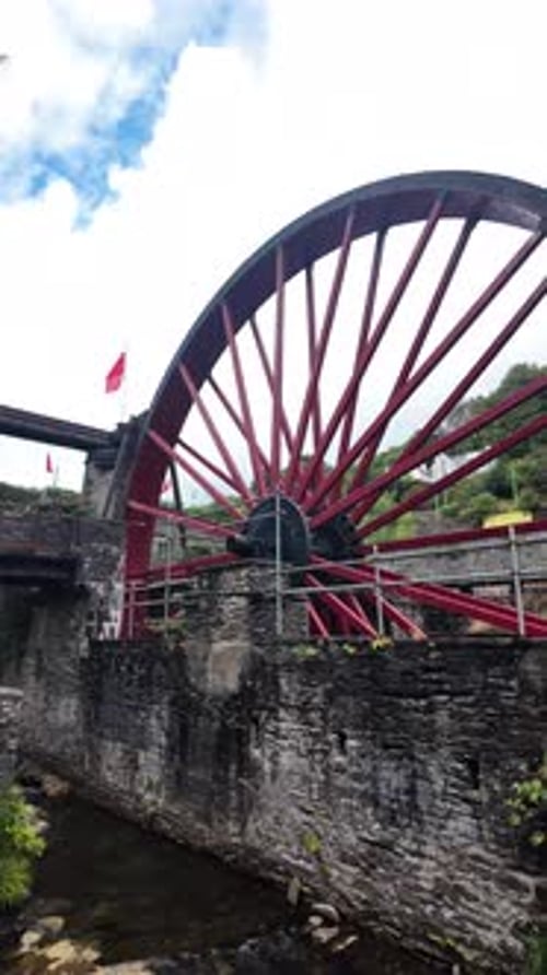 Red Water Wheel At Historic Mill Site With Stone Walls, Scaffolding, And Sky Above. vertical video