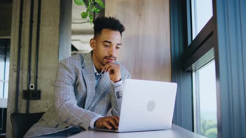 A Focused Young Man is Diligently Working on His Laptop in a Modern Office Setting Showcasing