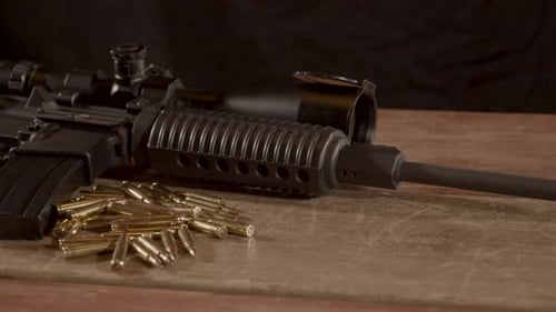Wide dolly in of AR-15 with a lot of ammunition lying on wooden surface