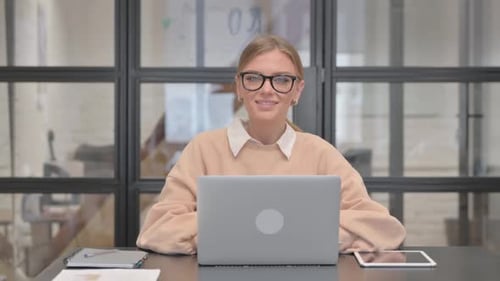 Young Woman Smiling at Camera while Working on Laptop in Office