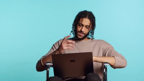 Man in Wheelchair Chatting with Friend Over Internet Videocall Using Laptop
