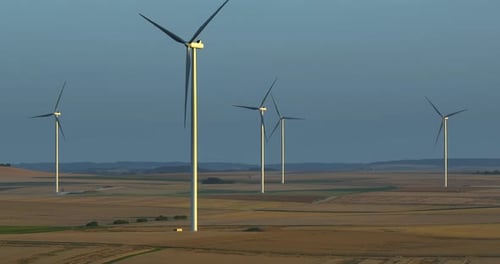 Alternative Energy Large Wind Turbines with Blades in Field Aerial View Bright Orange Sunset Blue