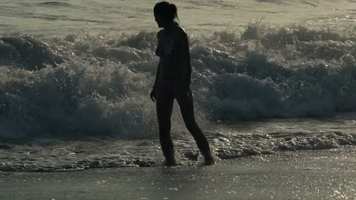 Young woman splashing playfully in the sea at sunset enjoying summer vacations