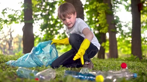 Boy collecting plastic garbage in a container in a polluted park, recycling signs on T-shirt. Slow m