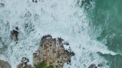 Aerial Video of Rugged Cliffside Surrounded By Strong Waves Foamy Water and Turquoise Ocean