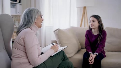 Verstörtes kleines Mädchen spricht mit einem Therapeuten über psychische Probleme in Innenräumen