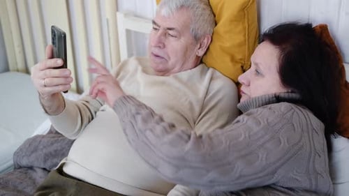Senior Couple Relaxing in Bed Looking at Phone