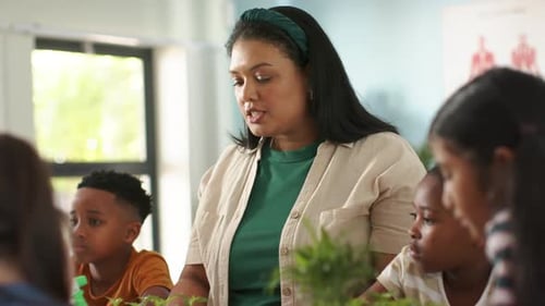 African American teacher looking left, speaking, guiding students with potted plants, green bottle