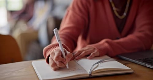 Person Writing in Notebook at Desk with Laptop