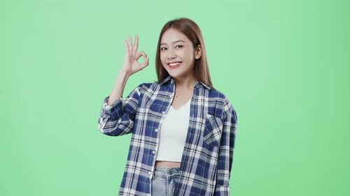 Glückliches schönes asiatisches Mädchen macht ein OK-Handzeichen und lächelt auf Chroma-Key-Hintergrund.
