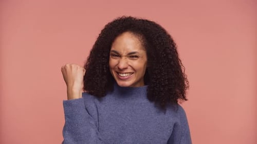 Excited Woman Celebrating Success with Fist Pump on Pink