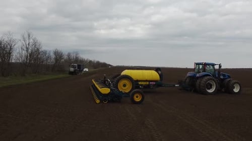 Blue tractor with yellow seeder working on the field in Ukraine OA