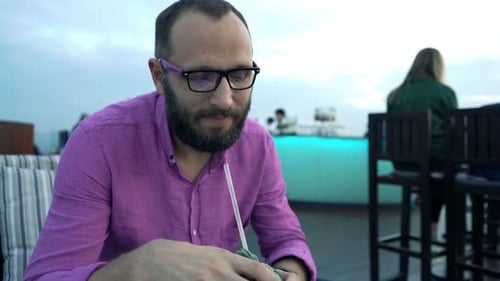 Young, Happy Man Relaxing and Drinking Cocktail on Terrace in Bar 30s