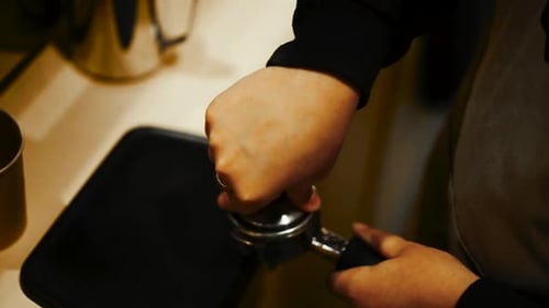 Close up high angle shot of barista pressing down on coffee grounds within portafilter (or group han