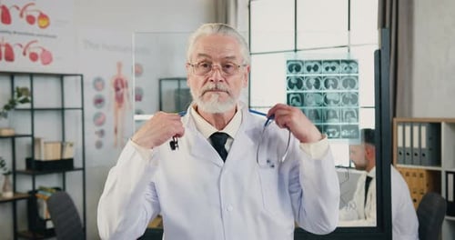 Attractive doctor putting on his stethoscope around his neck looking into camera in modern hospital