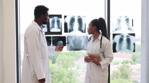 Male and Female Doctors Consulting Near Xrays in Modern Clinic