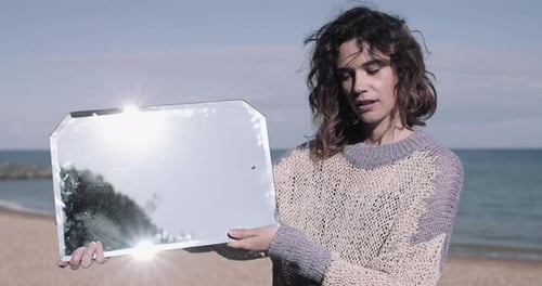Jeune femme adulte reflétant un miroir au bord de la mer.