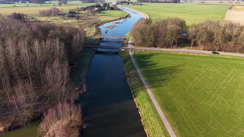 An aerial drone view of a calm canal cutting through a vibrant green rural landscape featuring small