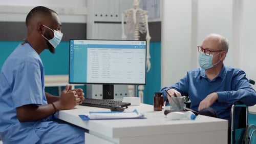 Doctor Consults Patient in Wheelchair in Hospital Office