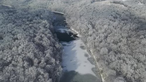 Reveal Frozen River with Ice and Snow Covered Forest Landscape, Winter Wilderness, Aerial