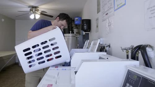 Man holding laundry basket and loading dirty clothes into the washing at an apartment complex.