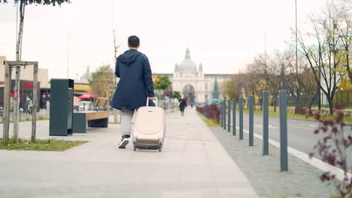 Asian male tourist going with a bag or pulls a suitcase down a city street. A man arriving in a new