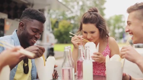 Friends eating takeout food by food truck