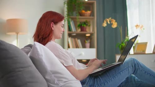 Woman Uses Laptop While Relaxing on Couch Indoors