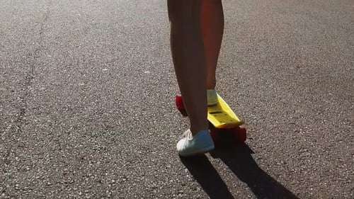 Teenage girl feet riding modern cruiser skateboard on road in slow motion