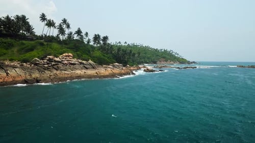 Aerial Reveals Tropical Island Coastline with Waves Crashing Against Rugged Rocks Fringed By Dense